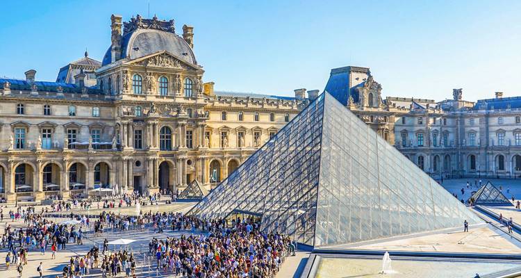 Iconic Louvre Pyramid surrounded by crowds in the courtyard of the historic museum palace