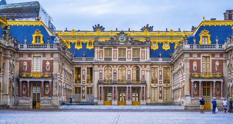Opulent front façade of the Palace of Versailles with blue and gold rooftops and ornate windows