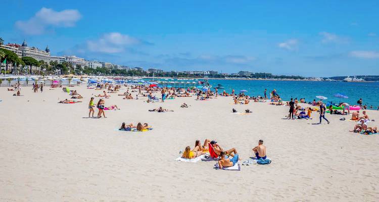 Wide sandy beach in Cannes crowded with sunbathers under a clear summer sky