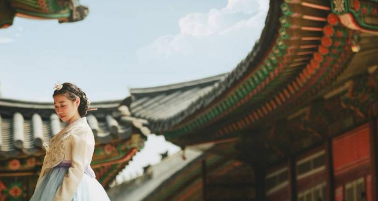 Une femme en hanbok traditionnel à côté d'un bâtiment orné dans un temple coréen.