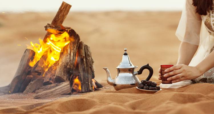 Una configuración tradicional de té marroquí con una tetera de plata y fogata en el desierto.