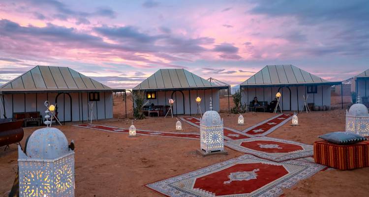 Un campement du désert magnifiquement éclairé au coucher du soleil avec des tentes décorées.