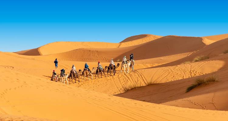 Rangée de personnes montant des chameaux sur des dunes de sable sous un ciel bleu dégagé.