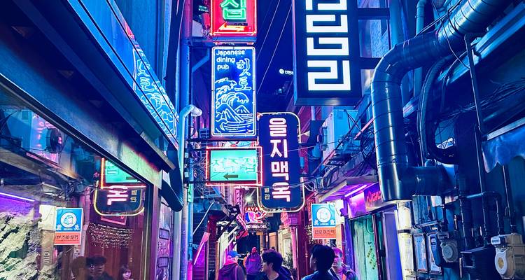 Ruelle étroite en Corée illuminée par les enseignes lumineuses colorées de restaurants et de bars au néon, tandis que des personnes marchent sous les lumières.