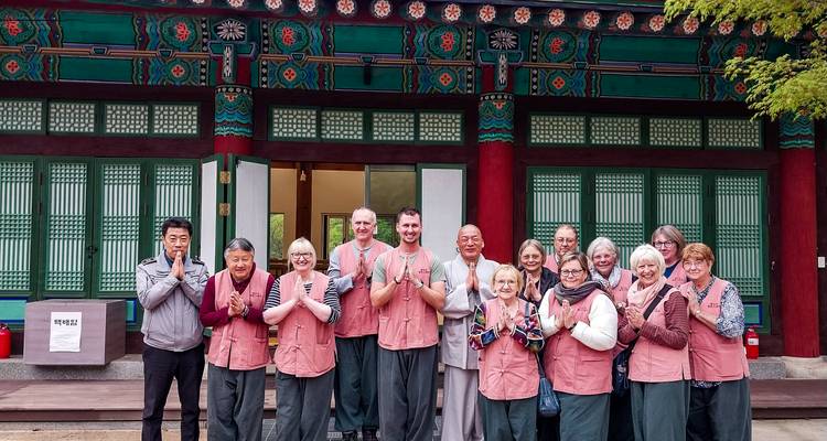 Un grand groupe de touristes en vêtements assortis de séjour en temple pose et sourit devant un hall de temple coréen aux poutres peintes.