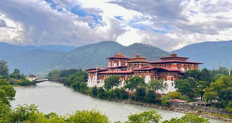 Monastère bhoutanais traditionnel au bord d'une rivière avec des montagnes en arrière-plan.