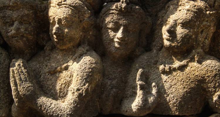 Close-up of ancient stone reliefs depicting praying figures on a historic Javanese temple wall.