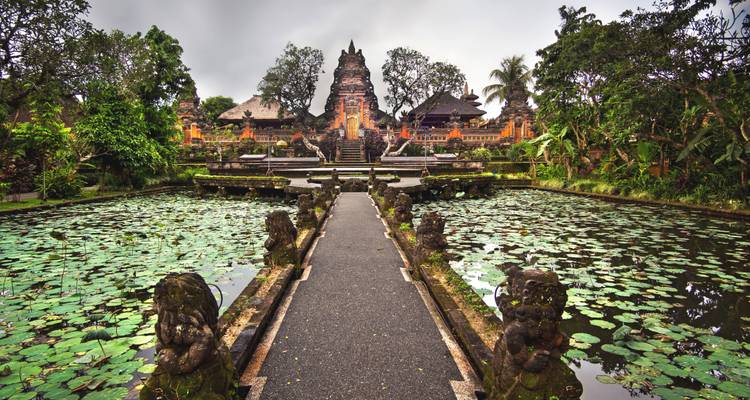Symmetrical pathway over a lotus-covered pond leading to an ornate Balinese temple.
