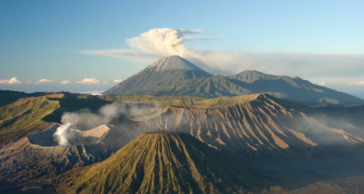 Clear morning view of Mount Bromo and surrounding ridges under a blue sky with drifting volcanic smoke.