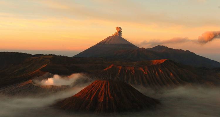 Fiery sunrise over the Mount Bromo volcanic complex with steaming craters and mist-filled valleys.