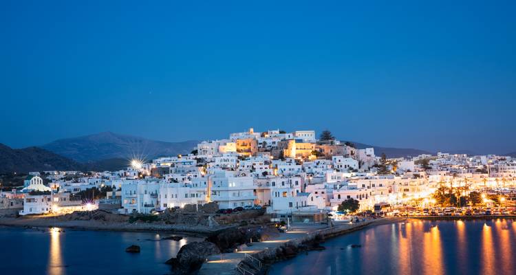 Witgekalkt bergstadje dat verlicht is tijdens het blauwe uur naast kalme havenwateren