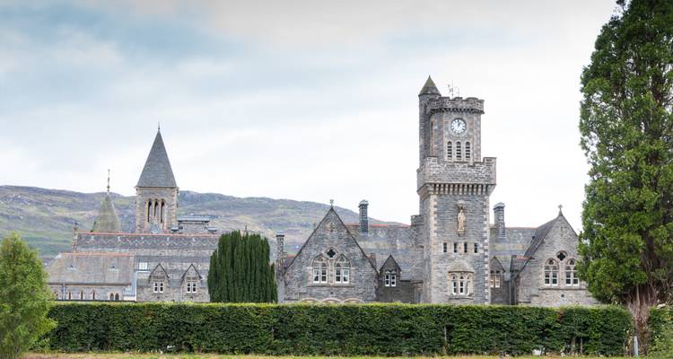 Bâtiment historique en pierre avec tour d'horloge sous un ciel nuageux.
