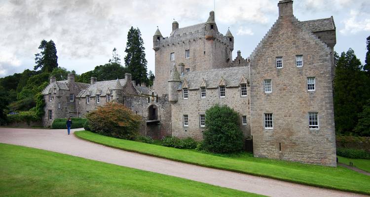 Vieux château entouré de verdure sous un ciel nuageux.