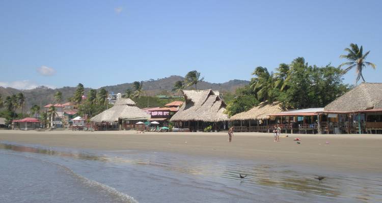 Strand met hutten en mensen die langs de kust wandelen.