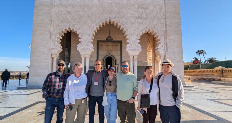Tour group posing before ornate marble mausoleum entrance with horseshoe arches in Rabat.