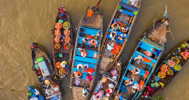 Colorful overhead view of wooden boats packed with people and fresh produce at a bustling floating market.