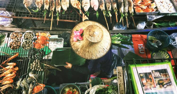 Overhead view of a market vendor grilling seafood and meats from a small boat stall.