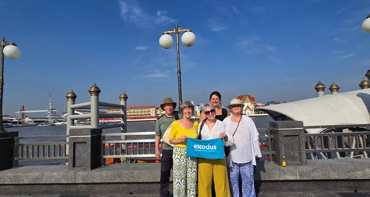 Travellers pose with an Exodus banner on a riverside promenade under a bright blue sky.