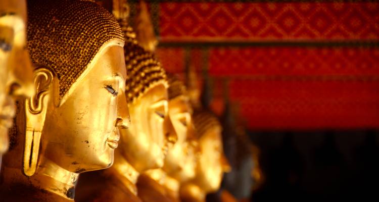 Row of gilded Buddha statues in warm light with a red patterned ceiling above.