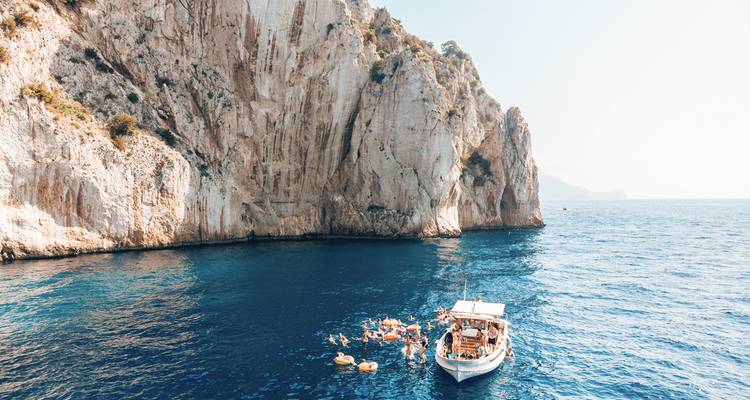 Zwemmers bij een boot in helder blauw water met steile kliffen.