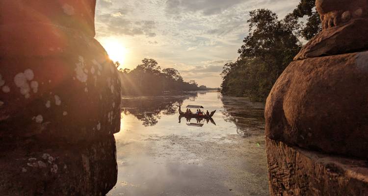 Une petite barque dérive sur les eaux réfléchissantes d'une douve au lever du soleil, encadrée par des sculptures en pierre anciennes.