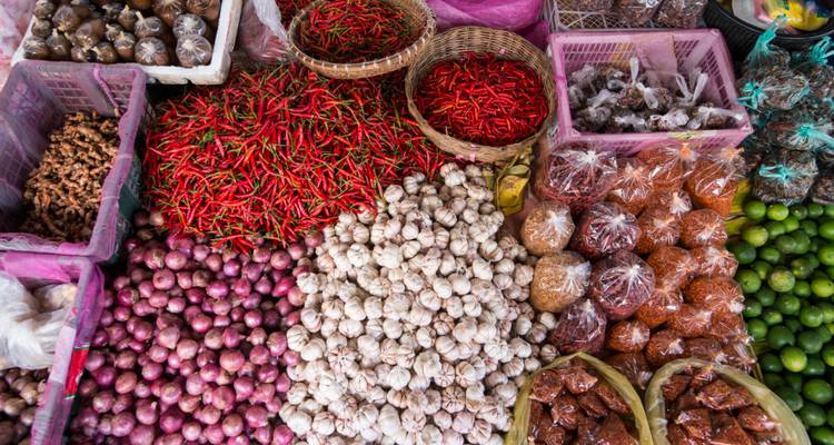 Affichage coloré de produits du marché incluant des piments rouges, de l'ail, des échalotes, des citrons verts et des épices dans des paniers.