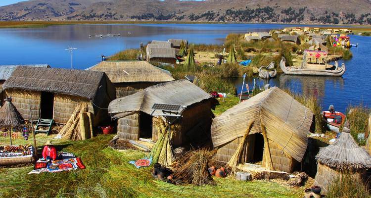 Islas de juncos y cabañas tradicionales en un lago con montañas como telón de fondo.