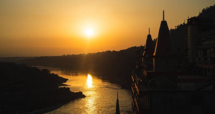 Vue du coucher de soleil sur une rivière avec des silhouettes de temples au premier plan.