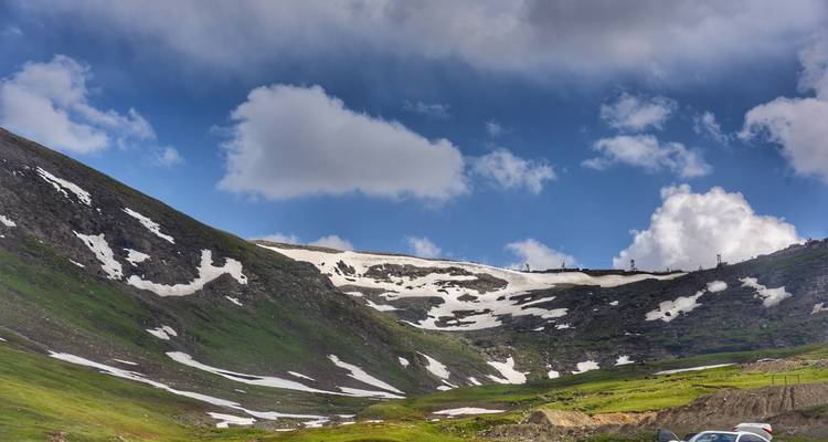 Vallée alpine élevée avec des poches de neige tardive, des prairies vertes et des nuages spectaculaires dans le nord du Pakistan.