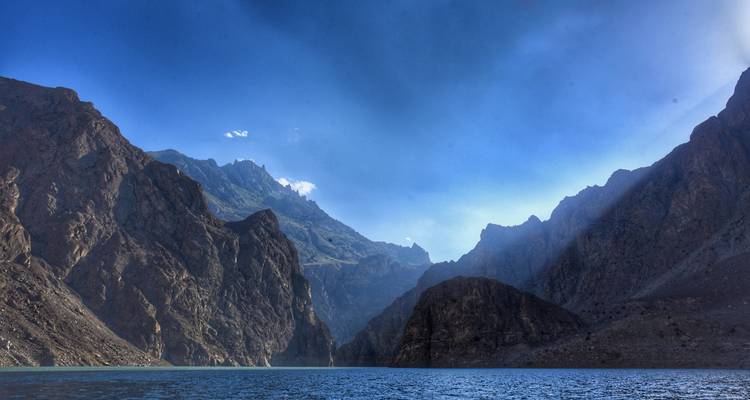 Lac alpin bleu profond encadré par d'imposantes falaises escarpées de la chaîne du Karakoram sous un ciel dégagé.