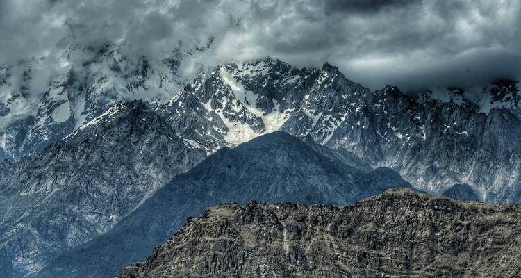 Gros plan dramatique de pics déchiquetés enneigés partiellement enveloppés de sombres nuages d'orage dans le Karakoram.