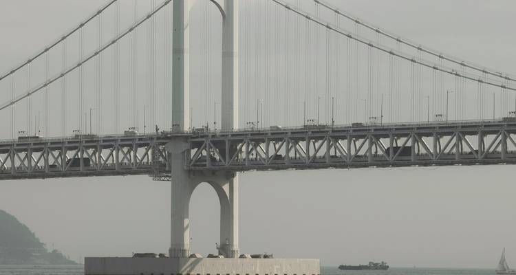A large suspension bridge crossing a body of water with a ship passing underneath.