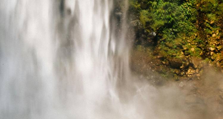 Détail en doux flou d'une cascade impétueuse avec brume et paroi rocheuse couverte de mousse.