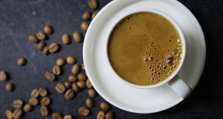 Vue de dessus d'une tasse d'espresso sur une soucoupe blanche avec des grains de café dispersés sur une surface sombre.