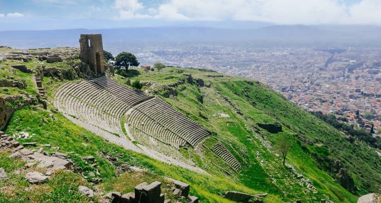 Ancient amphitheater on a hillside with a view of a city.