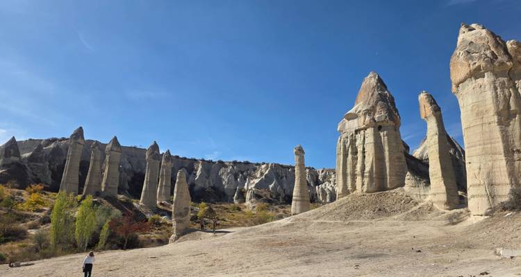 Vast landscape of towering fairy chimneys under a blue sky with a lone visitor for scale.