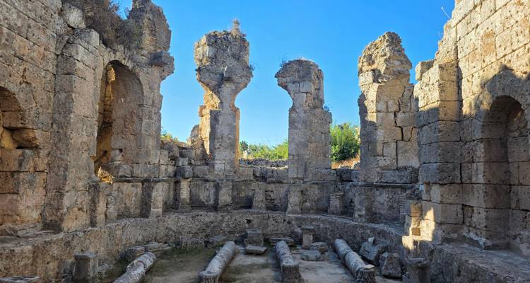 Ancient stone walls and columns of a Roman bath ruin lit by bright afternoon sun.