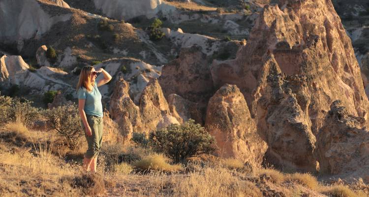 A woman shades her eyes while gazing over Cappadocia's sunlit ochre rock formations.