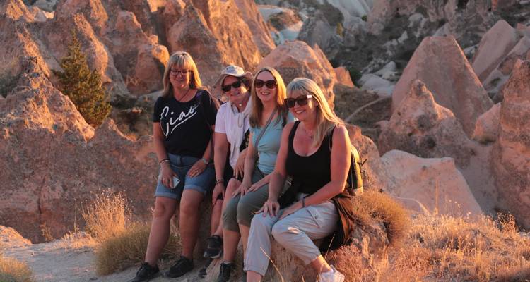 Four friends sitting on sun-warmed rocks smiling during sunset in Cappadocia.