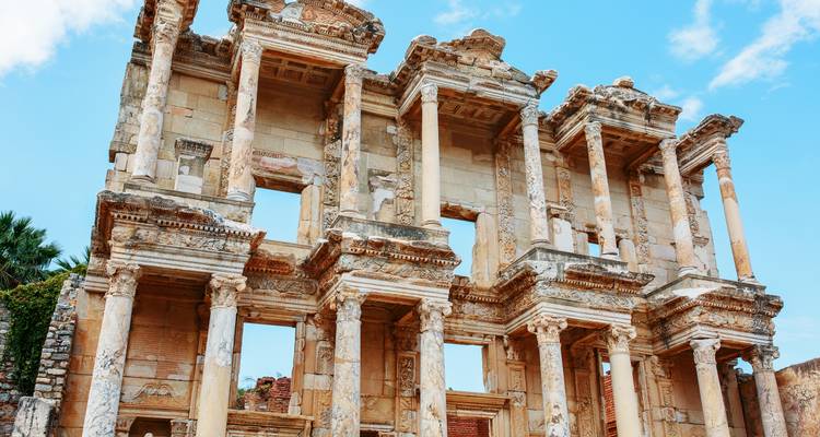 Ancient Roman library ruins with detailed columns and architecture under a blue sky.