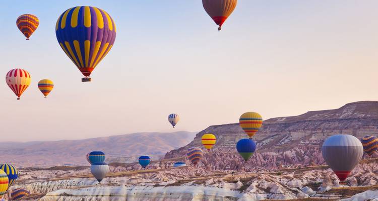 Multiple colorful hot air balloons floating over a rocky landscape.