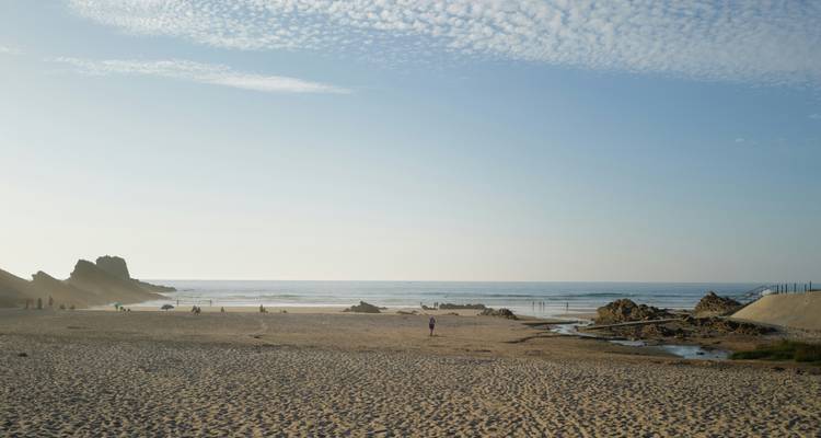 Large plage de sable avec quelques visiteurs éparpillés sous un ciel dégagé.