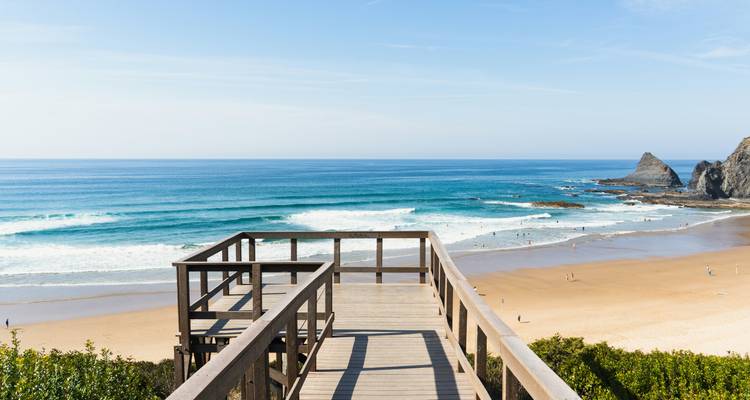 Passerelle en bois menant à une plage avec des vagues et un ciel dégagé.