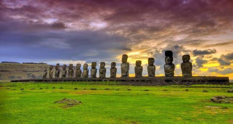 Long row of moai statues on Easter Island silhouetted against a dramatic purple and orange sky.