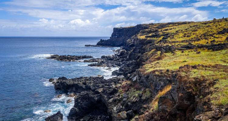Rocky volcanic cliffs plunge into deep blue ocean along a rugged Easter Island coastline.