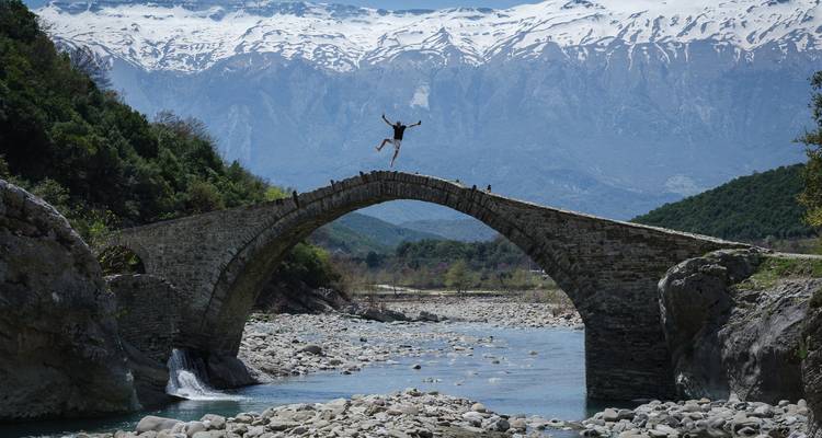Personne sautant sur un ancien pont de pierre au-dessus d'une rivière.