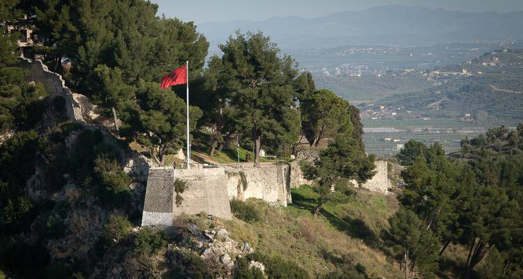 Fort avec drapeau albanais surplombant une vallée.