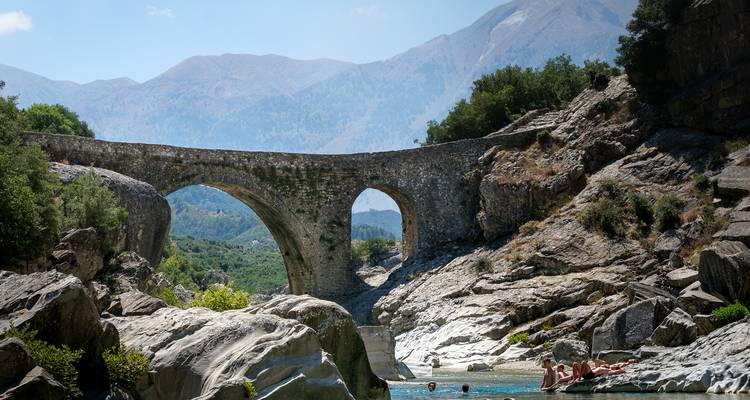 Pont de pierre sur une rivière avec des gens qui nagent.