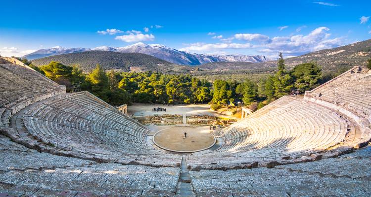 Panoramischer Blick auf das antike Steintheater von Epidaurus, eingerahmt von bewaldeten Hügeln und entfernten schneebedeckten Gipfeln