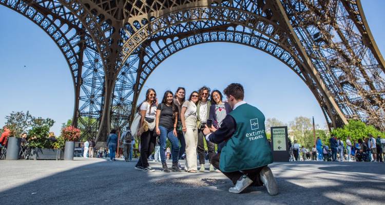 El grupo de turismo posa para una foto bajo los enormes arcos de hierro de la Torre Eiffel.